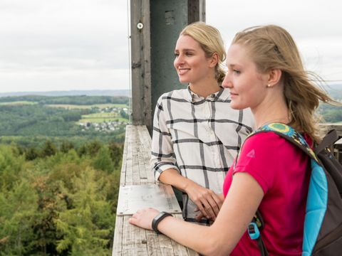 Zwei Frauen in Wanderkleidung stehen auf einem Aussichtsturm und blicken auf die weite Landschaft.